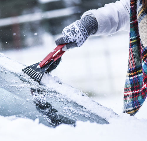 A person scraping the window of a frozen car windshield